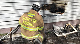 A fire investigator inspecting fire damage on the side of a house.