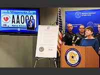 Barb Degnan speaks at a news conference where a broken heart license plate is displayed