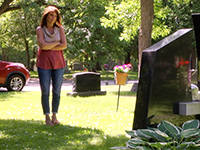 Photo of a mother looking at a headstone in a cemetery.
