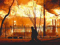 A firefighter walking in front of a burning home