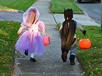 Two children in Halloween costumes running down a sidewalk
