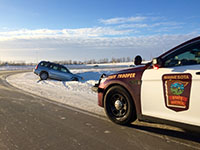 A car in a snowy ditch and a state patrol squad car parked on the edge of the road