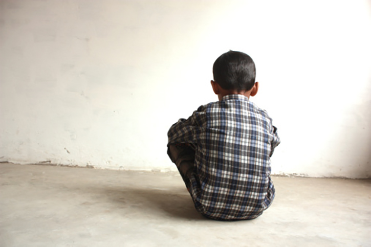Photo of a child sitting alone in a bare room.