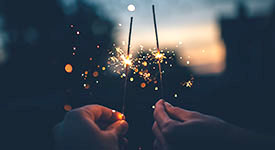 Two hands holding sparklers against the evening sky