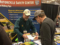 A motorcycle show visitor looks at a brochure with a staff member at the MMSC booth