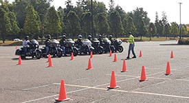 Motorcycle training participants lined up on motorcycles lined up by a field of traffic cones