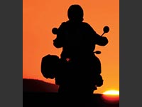 A motorcyclist riding toward a sunset