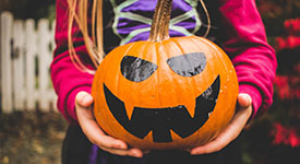 A person holding a pumpkin decorated with eyes and a smile