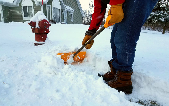 A person shoveling a path to a fire hydrant surrounded by snow.