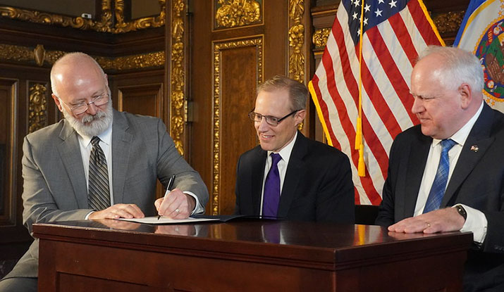 DPS Commissioner Bob Jacobson signing his name as Secretary of State Steve Simon and Gov. Tim Walz look on during his swearing in.