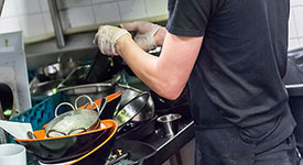 A person washing dishes in a restaurant kitchen.