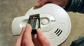 Hands place a battery inside a smoke alarm