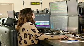 A female 911 dispatcher sitting at her desk looking at computer monitors.