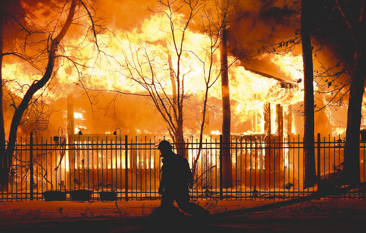 A firefighter walking in front of a burning home