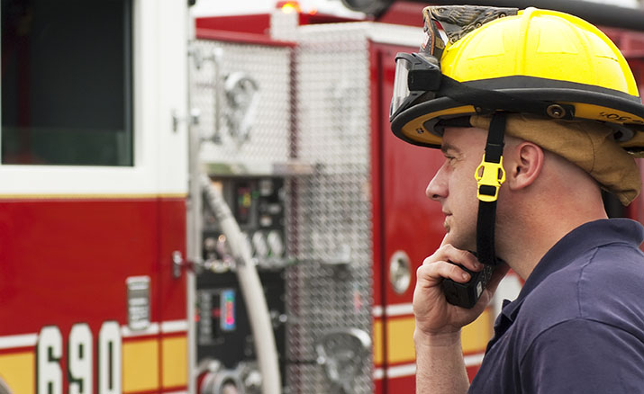 A firefighter holding a radio while standing near a fire truck