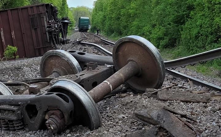 A train car on its side and parts scattered on the ground after a derailment
