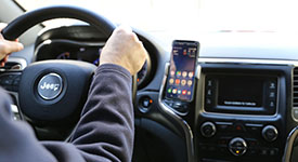 A driver with their hands on the steering wheel and a smartphone in a dash mounted holder