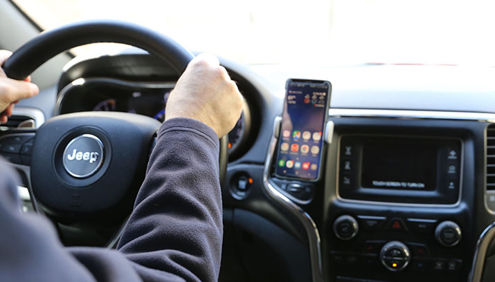 A driver with their hands on the steering wheel and a smartphone in a dash mounted holder