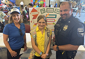 Minnesota Rep. Kristin Robbins and Corcoran Police Sgt. Pete Ekenberg with Makenna Prevost standing in front of a project display board.