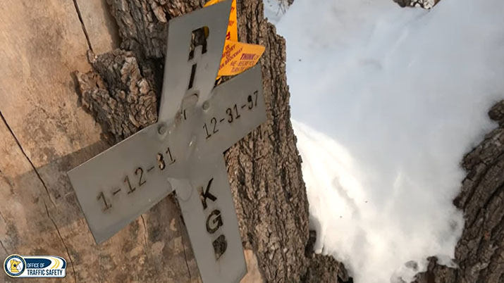 A metal cross on a tree at the crash site. The cross has Kevin's initials along with birth and death dates