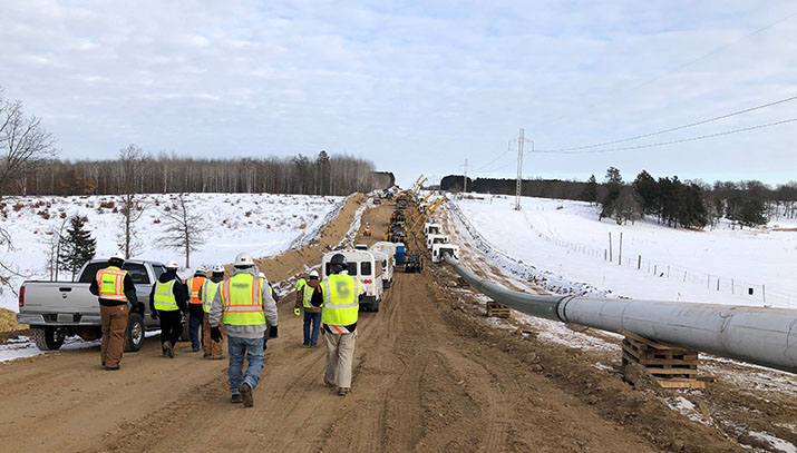 Workers walk along a road next to a section of the new Enbridge Line 3 pipeline