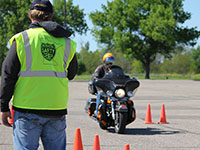 A motorcyle training instructor watches a student navigate through a training course on a motorcycle