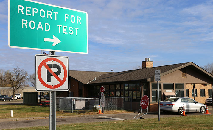 Report for Road Test sign with a driver exam station building in the background