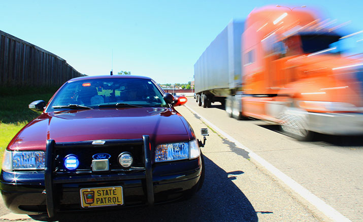 A squad car on the shoulder of the road and a semi passing without moving over