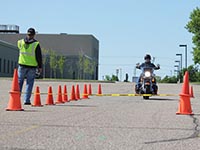A motorcycle training instructor watches as a rider enters a series of traffic cones