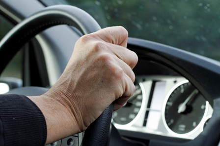 driver with hands on steering wheel of car