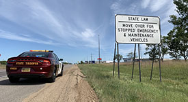 A State Patrol squad car parked near a move over for stopped emergency vehicles sign along a road
