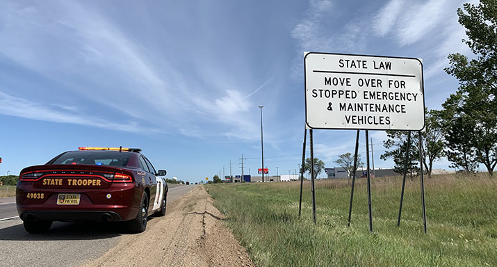 A State Patrol squad car stopped on the shoulder of the road next to a highway sign informing drivers of the Move Over Law