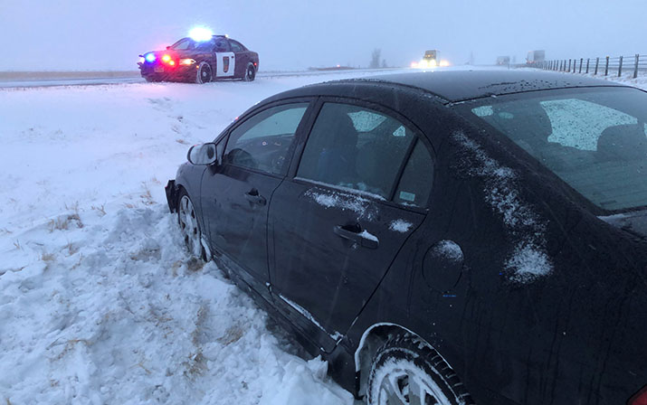 A car in a snow-filled ditch and a State Patrol squad car on the shoulder of a highway