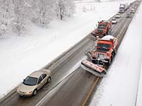 Two snow plows and other vehicles on a slushy, snow-lined road