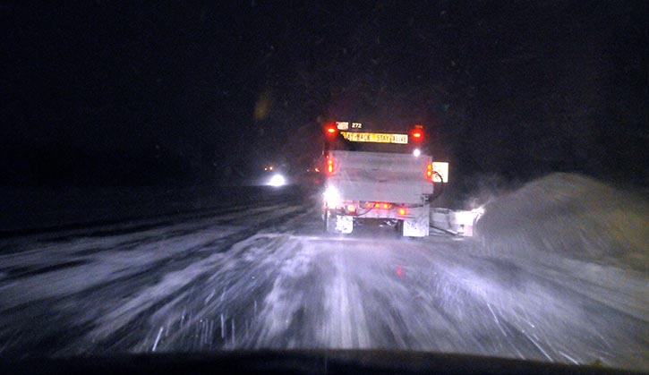 Photo of a snowplow working in front of a vehicle.