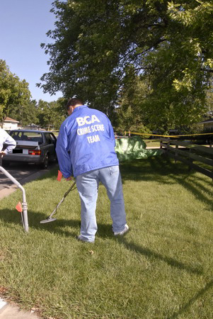 a member of the crime scene team using a metal detector to locate cartridge cases in grass