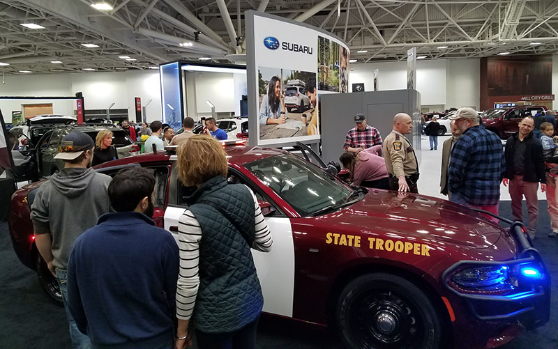 Auto show visitors walking by a squad car on display.