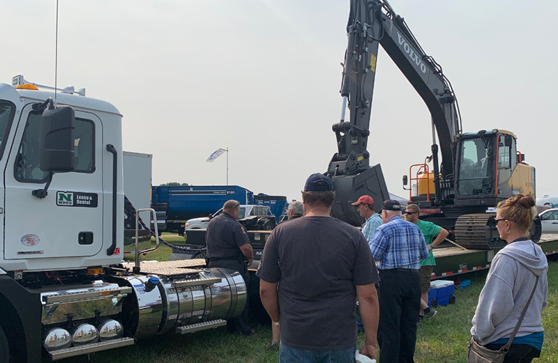 A commercial vehicle inspector speaking with people next to a semi-trailer at an event.