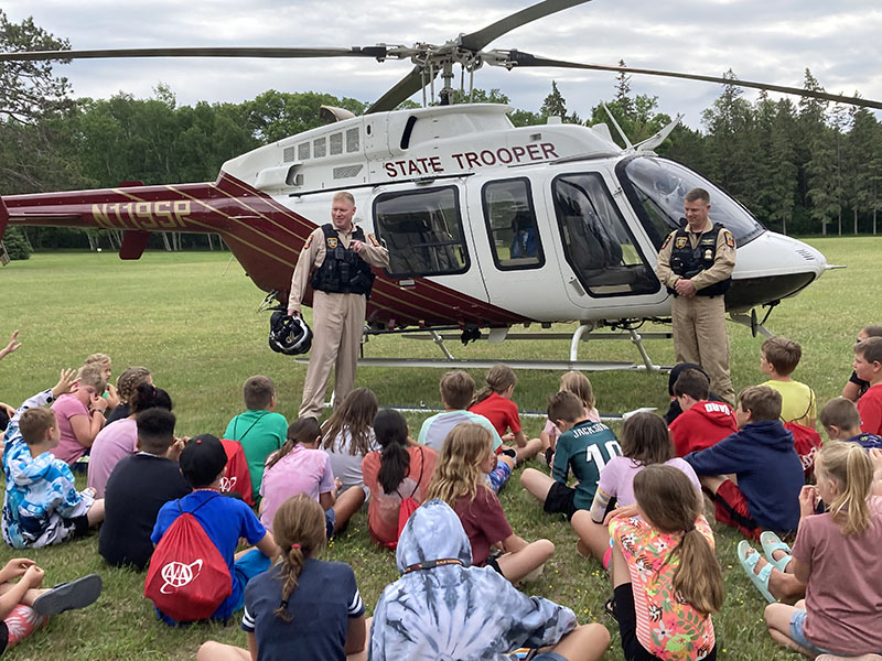 Two State Patrol pilots standing in front of a helicopter and talking to a group of children.