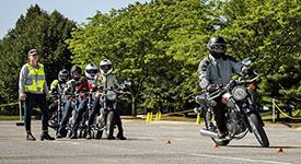 A motorcyclist navigating a training course as other riders watch.