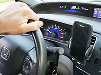 A hand on a steering wheel with a phone in a vent mount