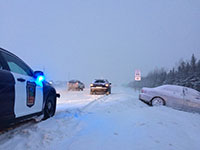 A winter car crash scene with a state patrol squad parked on the shoulder of the road