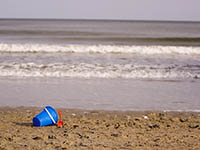 A plastic bucket and shovel on a beach with waves in the background