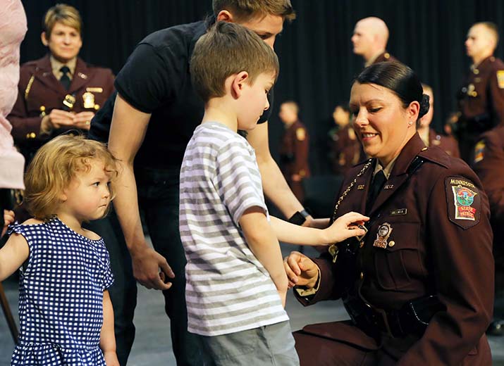 A Minnesota State Patrol Academy graduate’s young son pins on her badge at graduation. 