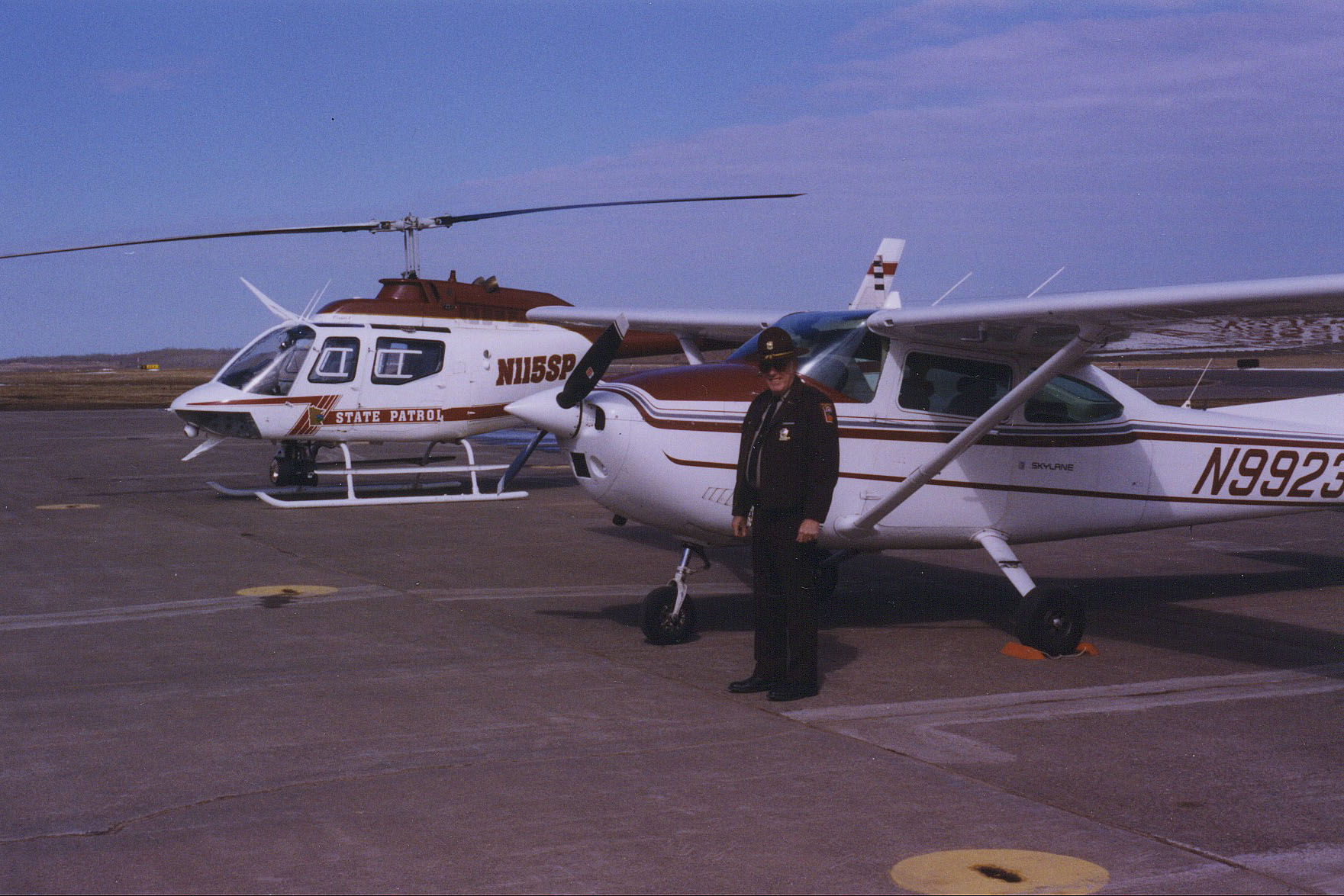 A trooper standing next to a fixed-wing aircraft and a helicopter in the background