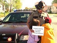 Two children hug a state trooper, who is holding a sign that reads, "My family is expecting me for dinner. #MoveOver.