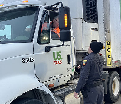 A commercial vehicle inspector standing next to a semi-truck and talking to the driver