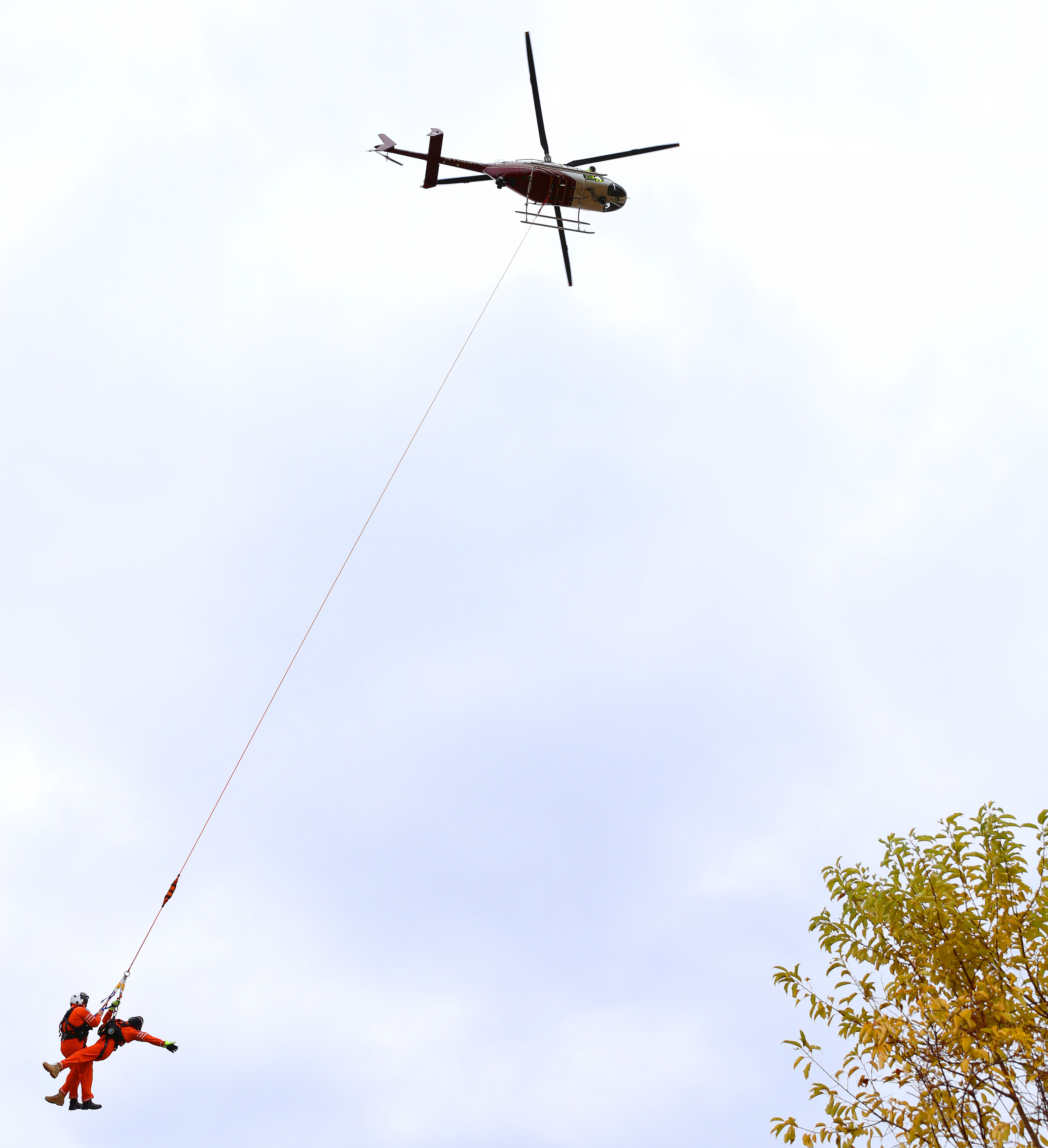 Two people in orange suits are rescued by a helicopter during a training exercise.